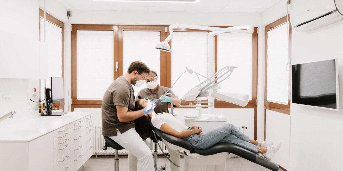 Ein Zahnarzt und seine Assistentin führen eine Behandlung an einer Patientin in einer modernen Zahnarztpraxis durch.