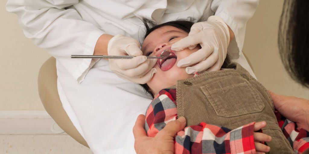 Zahnarzt untersucht Baby mit dentalem Spiegel während das Baby ruhig liegt.